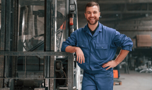 Leaning on the forklift. Factory worker in blue uniform is indoors